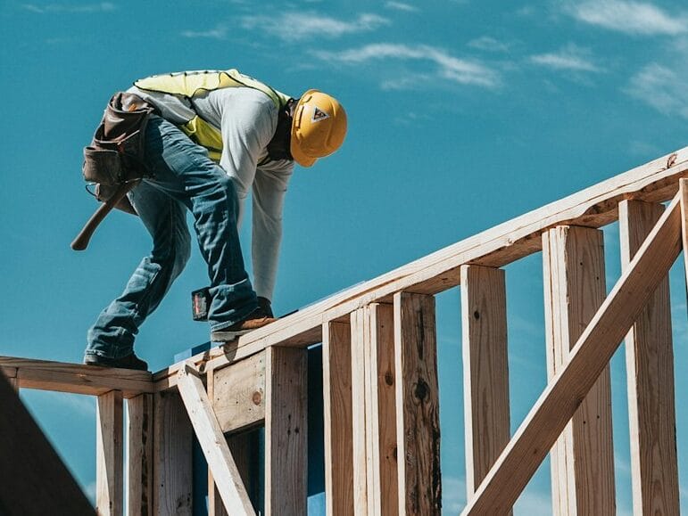 A man in a hard hat walking on wood framing while constructing a house.