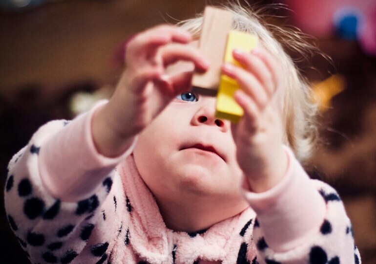 A baby holding two blocks.