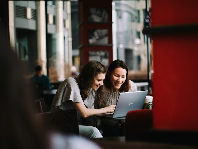 Two women viewing a laptop in an internet cafe.